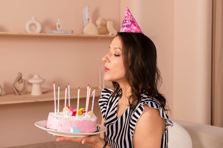 Beautiful brunette woman celebrating her birthday, dressed in a striped short dress and a birthday...