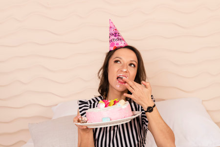 Beautiful brunette woman celebrating her birthday, dressed in a striped short dress and a birthday...