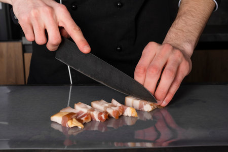 A Cook in a black uniform in the kitchen with ingredients prepared for cooking. Chef making an...