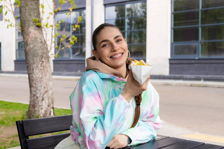 Young Slim brunette girl eating fast food hotdog or burger outdoor on the street.