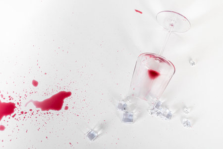 A broken glass with Wine stains and ice cubes spilling against a white background.の写真素材