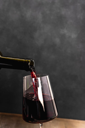 Wine is pouring into a glass against a dark gray or black background.の写真素材