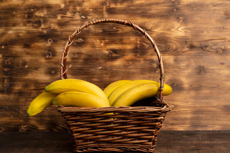 Bunch of bananas in a wicker basket against a wooden background.の写真素材