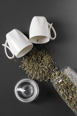 A white cup or mug and a glass jar are lying on their side with loose leaf tea spilled out. flat lay...