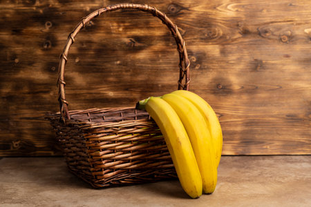 Bunch of bananas in a wicker basket against a wooden background.の写真素材