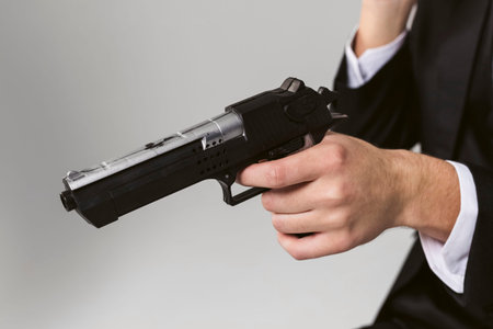 Close-up of a man in black souit holds a gun or pistol, isolated on white background.の写真素材