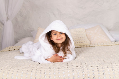 Adorable happy little girl in white bathrobe lies on a bed.の写真素材