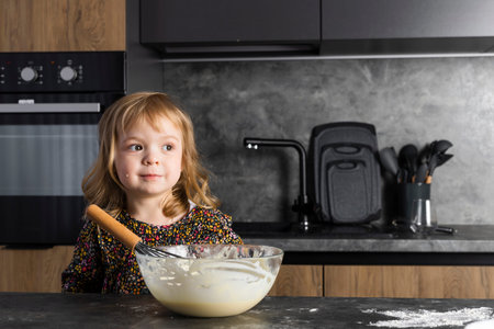 Portrait of a little cute girl helping her mother on a kitchen, mixing the dough.