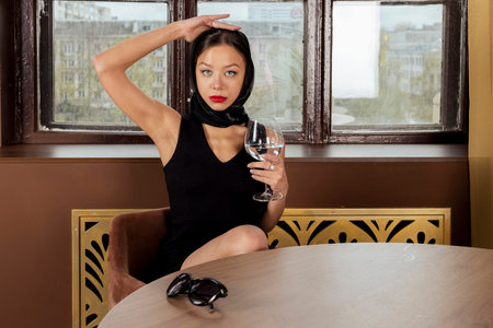 A famous businesswoman or celebrity, lady in a black dress and headscarf with a glass of water in a restourant.の写真素材