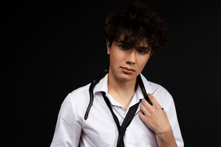Young handsome man in white shirt with a black snake crawling on his neck. Isolated on black background.の写真素材