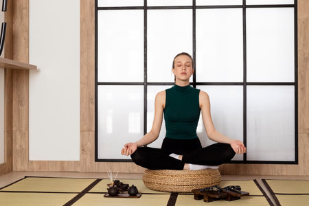 Young Slim brunette Girl practicing yoga, wearing sportswear. incense sticks and tea set lying on the floor. Indoor in a Japanese style studio.の写真素材