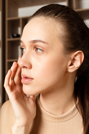 Tender Slim brunette Girl in beige top, using cosmetics, applying face cream. Indoor in a Japanese style studio.の写真素材