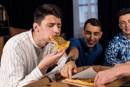 Small group of friends eating pizza with a big appetite, taking slices from the boxの写真素材