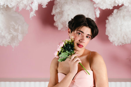 Close-up Portrait of a tender gay in a pink dress with flowers, bouquet. Glamour homosexual young guy with makeup posing in a girly outfit. head shot.の写真素材