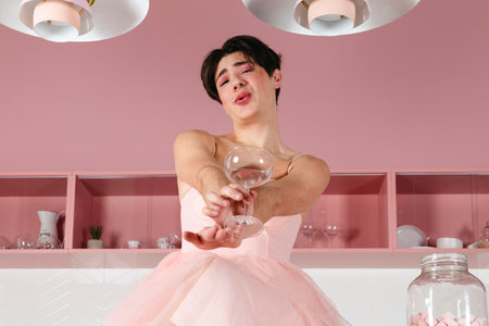 Portrait of a tender gay in a pink dress, drinking alcohol. Glamour homosexual young guy with makeup posing in a girly outfit.の写真素材