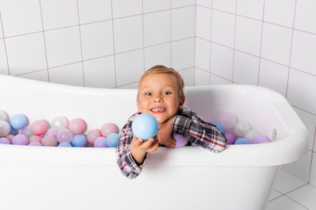 Little boy in a bath tube filled with plastic balls. Child peeking from pastel multi colored plastic balls for kids. top view.の写真素材