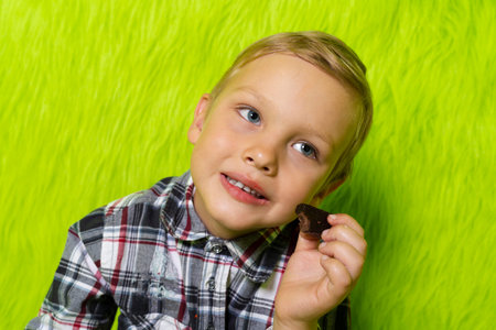 Little boy eats a lot of sweet food, glazed donuts and chocolate candies. Isolated on green furry background.の写真素材