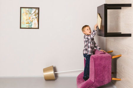 Little boy in the upside down room, reaching his hand to the table and book. Child standing on the wall of the room. flipped room.の写真素材