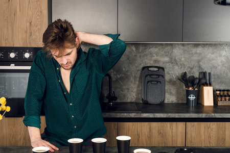 Sleepy man addicted to coffee cant stop drinking in the kitchen, many cups scattered around a table....