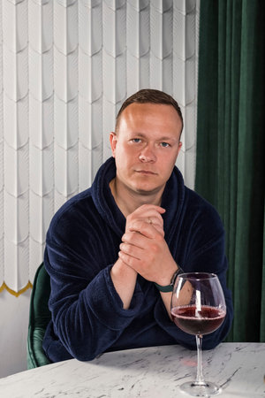 Portrait A homebody man in a blue bathrobe. A middle aged man with a glass of wine relaxing after...