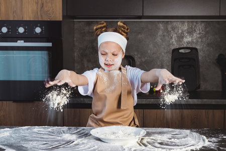 happy little girl in apron sprinkling flour on dough in kitchenの写真素材