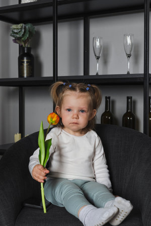 Cute, shy confused little girl holds a flower, looking at the camera.の写真素材
