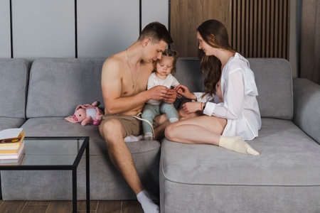 Happy family on sofa and in living room. father and mother playing with little daughter sitting on sofa at homeの写真素材