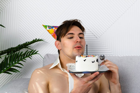 Shirtless man with a tie is celebrating his birthday, holds funny decorated cakeの写真素材
