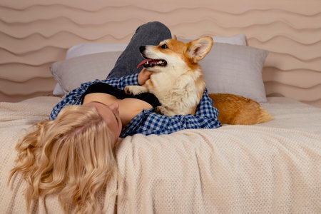 Attractive blonde hair girl and a Welsh corgi Pembroke dog are lying on the bed together.の写真素材