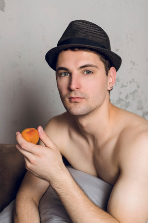 Portrait of a Handsome shirtless slim young man in a hat eating peach Or apricot.の写真素材