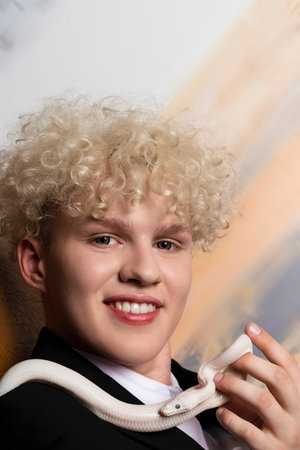 Stylish blonde haired young man and a Leucistic Ball Python. Pure white snake in businessman hands...