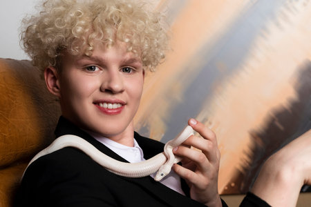 Stylish blonde haired young man and a Leucistic Ball Python. Pure white snake in businessman hands...
