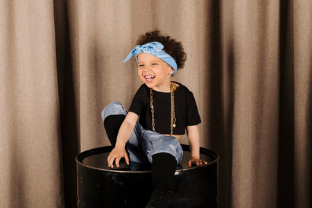 Cool Cute little girl wearing gold chains sitting on a metal barrelの写真素材
