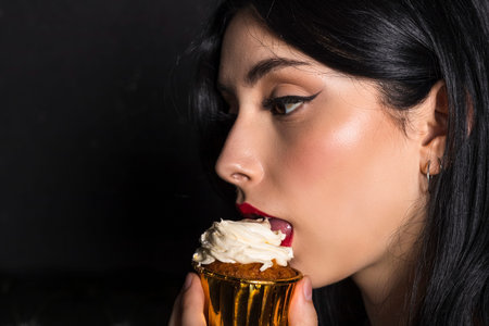 portrait Elegantly dressed young beautiful girl with black hair and dress celebrating 18th birthday. holds little cake with lit candle. isolated on black background.の写真素材