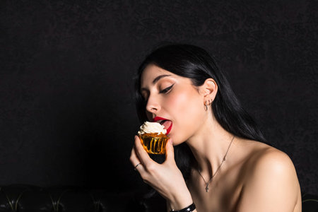portrait Elegantly dressed young beautiful girl with black hair and dress celebrating 18th birthday. holds little cake with lit candle. isolated on black background.の写真素材