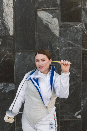 Female Fencer athlete wearing white fencing suit outfit and holding the sword, posing outdoors