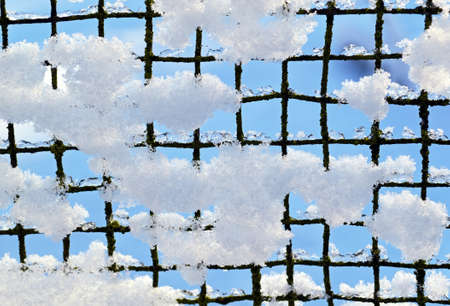 Snow on the fence of steel mesh on the sky backgroundの写真素材