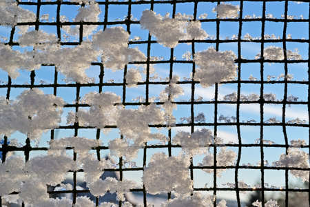Snow on the fence of steel mesh on the sky backgroundの写真素材