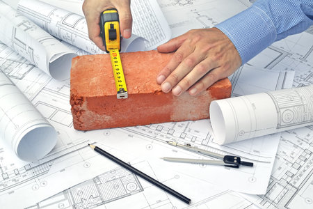 Hands of engineer working with the tool on project drawings background