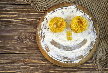 Photo of smiling faces from pasta and flour lying on a wooden tableの写真素材