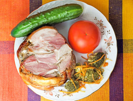 The big appetizing piece of smoked pork with vegetables is located on a table on a white plate.の写真素材