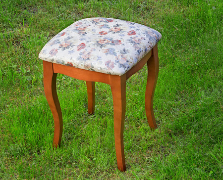 Beautiful stool in style of a retro with the soft seat upholstered with a gobelin. It is presented against a green lawn.の写真素材