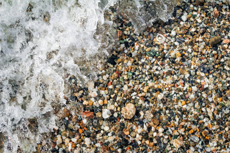 Small multi-colored sea stones on the beach, covered with transparent sea water.の写真素材