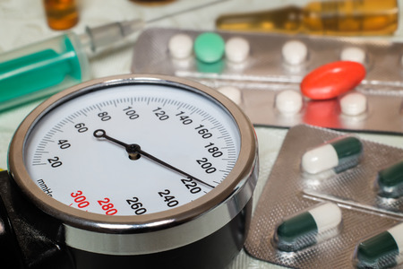 On the table is an apparatus for blood pressure measurement, which shows higher pressures. It's a hypertensive crisis. Near are medications to assist.の写真素材