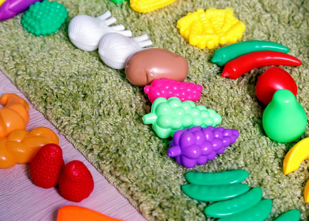Floor and carpet are various plastic children toys in the form of various vegetables and fruits: grapes, pear, strawberries, onions, peas, and others.の写真素材