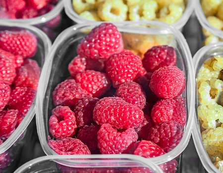 Ripe yellow and red raspberries in small containers for sale in the store.