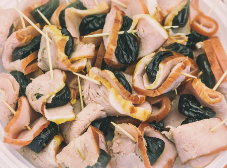 Appetizer of meat: slices of ham and prunes glued thin sticks. Presents closeup.