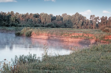 Beautiful calm river with the mist over the surface of the water at dawn by the light of the rising sun.の写真素材