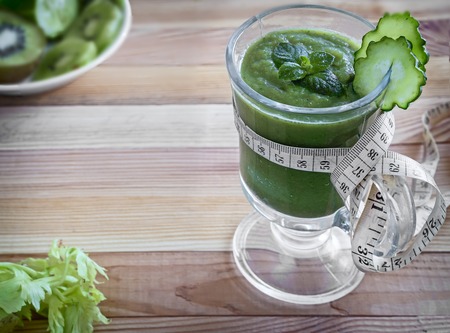 On the table in a glass vessel low-calorie smoothie made of cucumber, celery, apples and kiwi, designed for diet at weight loss.の写真素材