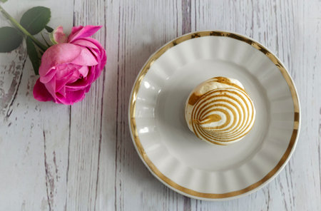 On a white plate is a delicious marshmallow, next to a rose. The view from the top.